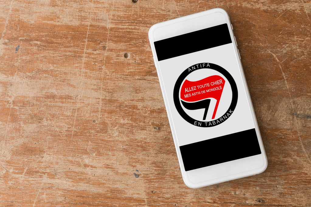 Sur un téléphone posé sur une table, l'image que Roxane veut se faire tatouer. Il s'agit de l'habituel logo antifasciste, mais avec le texte "ANTIFA EN TABARNAK" et "ALLEZ TOUTE CHIER MES ASTIS DE MONGOLS".